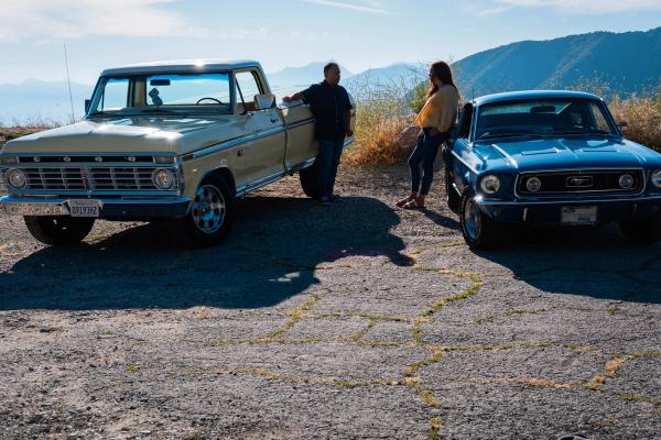 Couple standing between their two classic cars in the mountains
