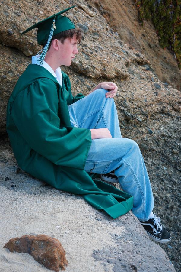 Graduate in his gown sitting on the rocks above the beach