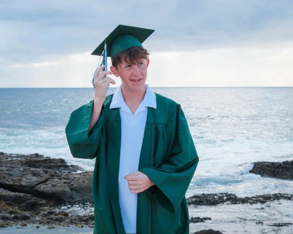 Graduate tipping his cap on the beach with the ocean behind him