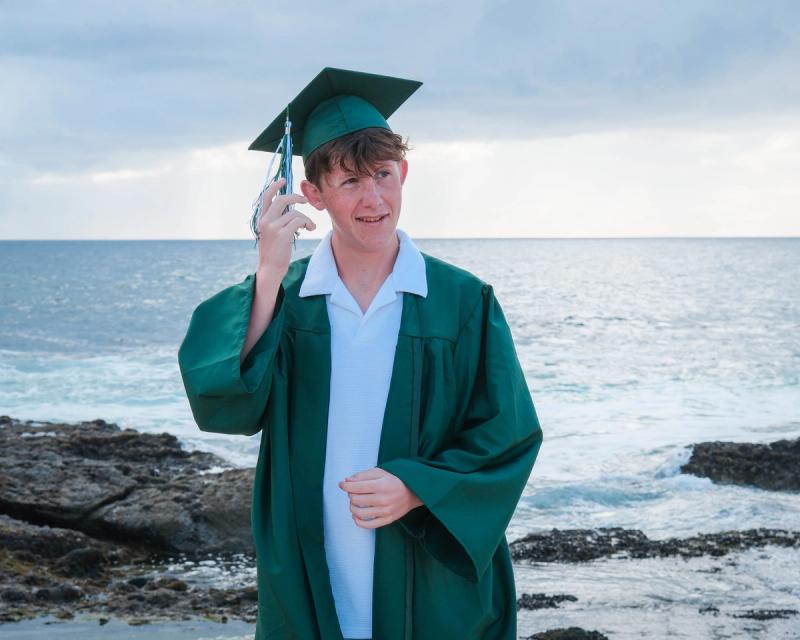 Graduate tipping his cap on the beach with the ocean behind him