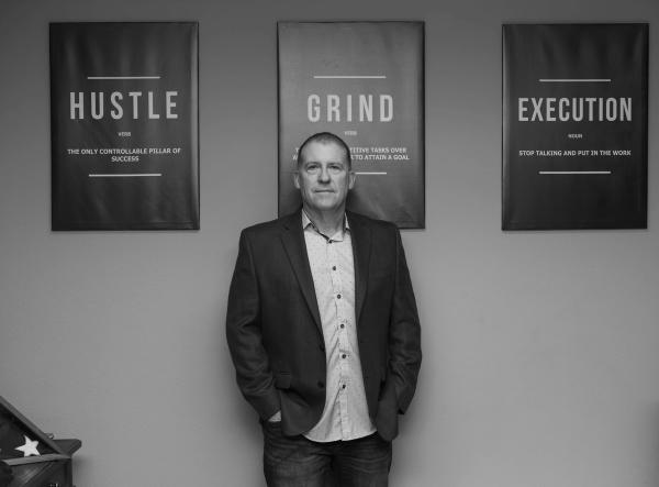 Black and white portrait of an executive in front of Hustle, Grind and Execution posters