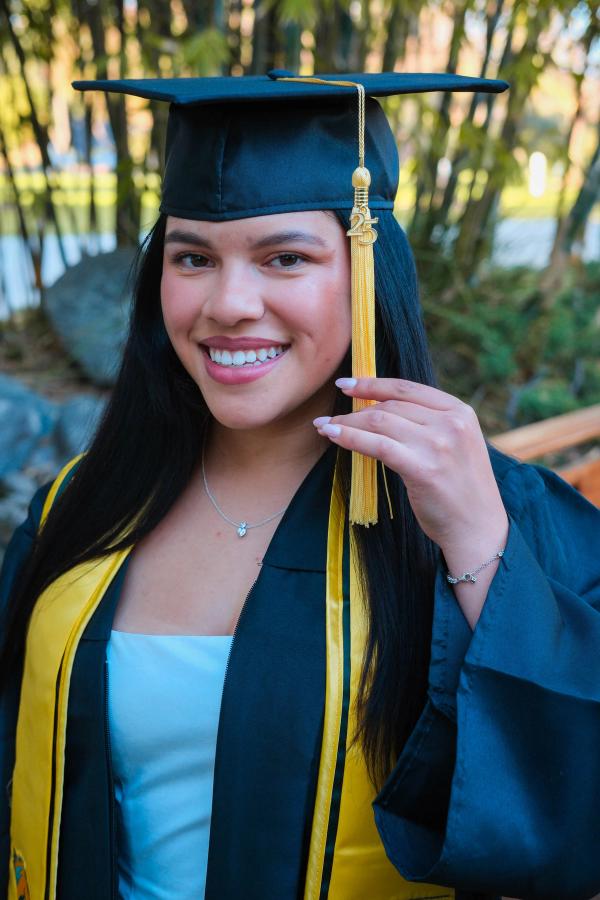 Graduate in cap and gown smiling and holding her tassel