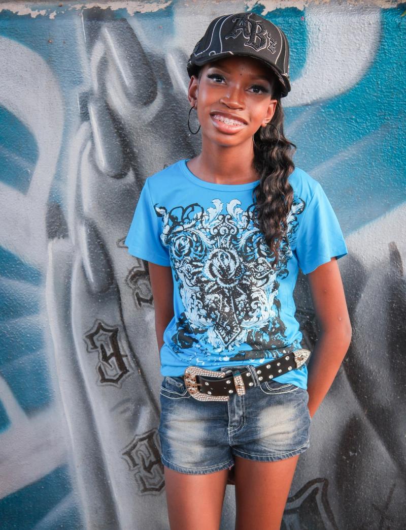 Girl in a bright blue tee and cap smiling against a gray street-art wall