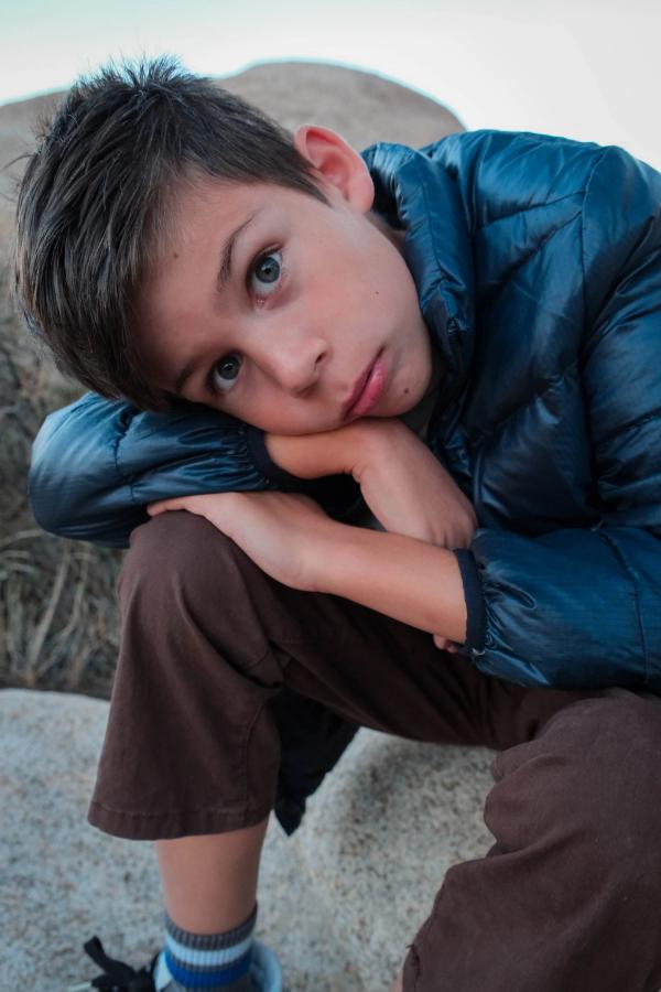 Boy in a blue puffer jacket resting his head on his arms on a boulder