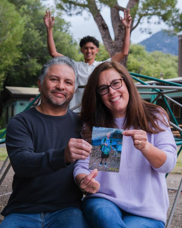 Parents holding up their son’s childhood photo as he cheers behind them