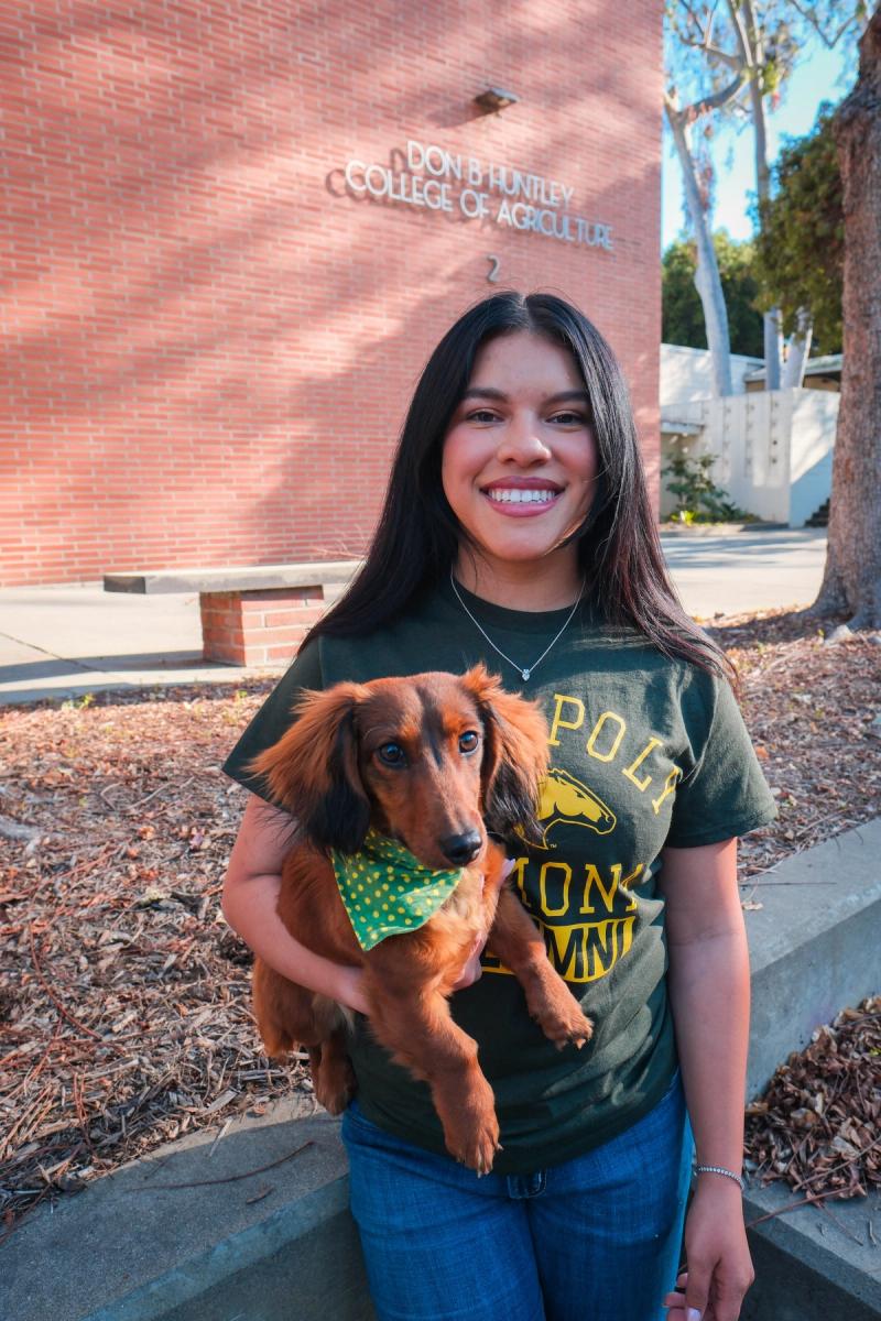 Smiling graduate in a Cal Poly Pomona T-shirt holding her dachshund
