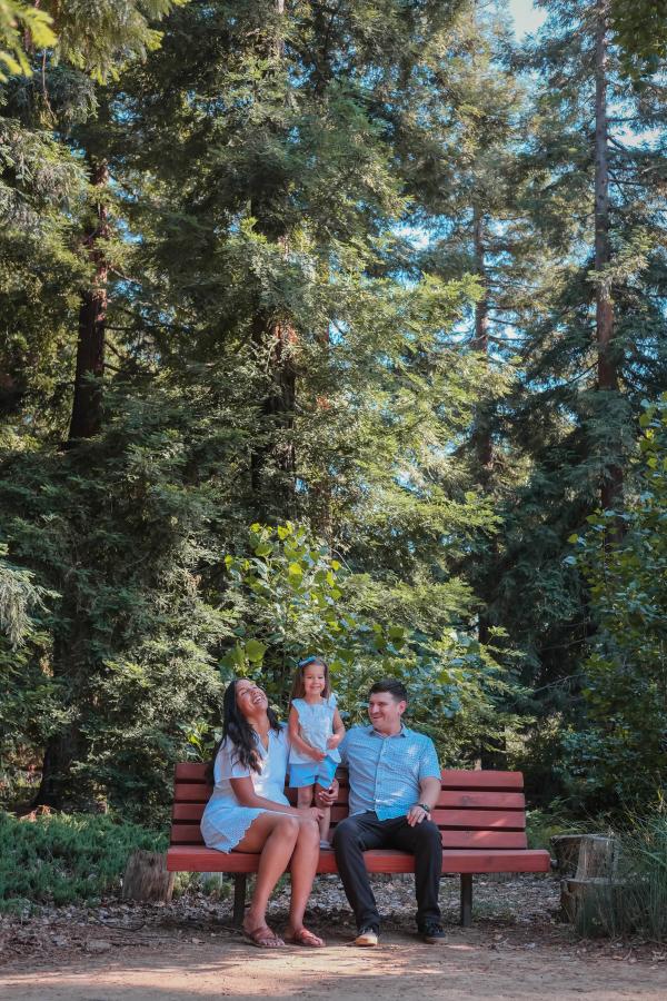 Family sitting on a red bench beneath tall redwoods