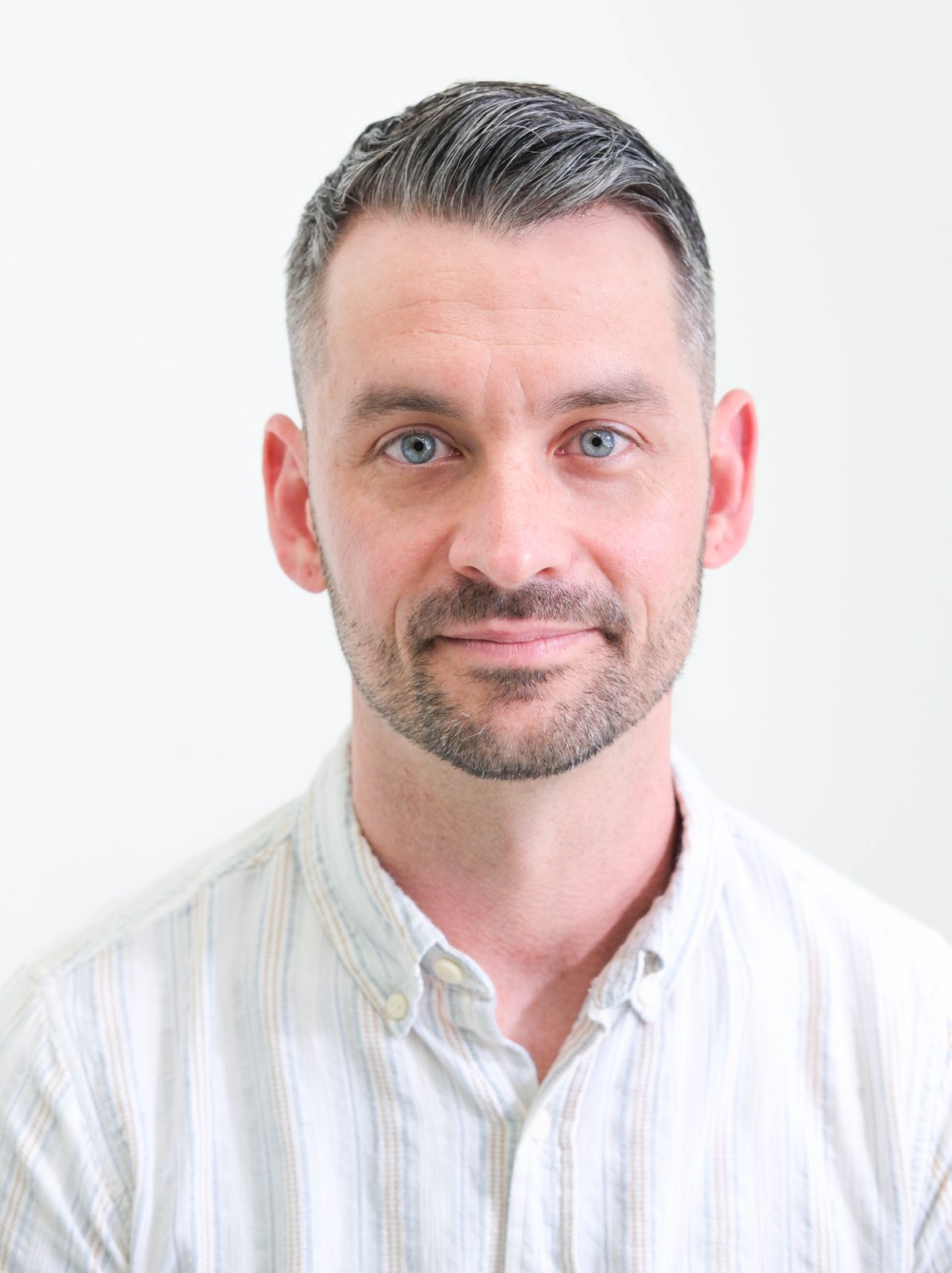 Professional studio headshot of a man in a light button-down shirt, looking directly at the camera