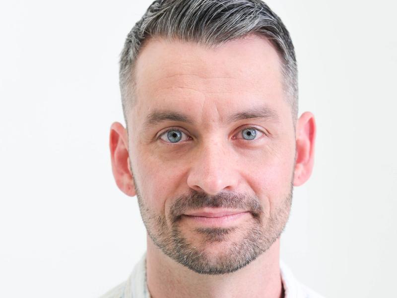 Professional studio headshot of a man in a light button-down shirt, looking directly at the camera