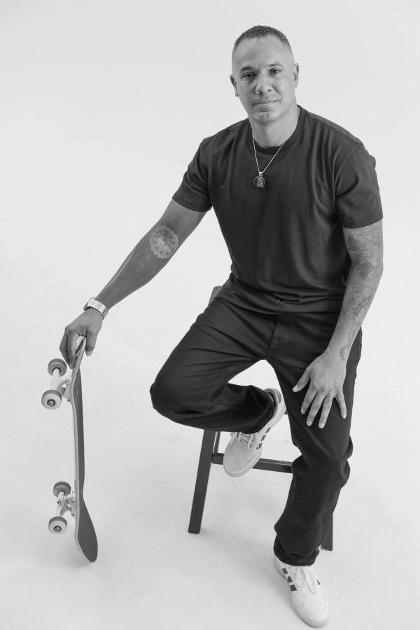 Man seated on a stool with one foot on a skateboard in the studio