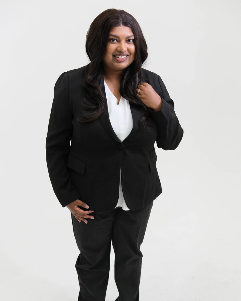 Full-length portrait of a woman in a black suit with her hand at her lapel