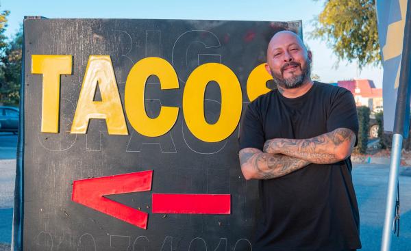 Owner leaning on a big yellow TACOS street sign