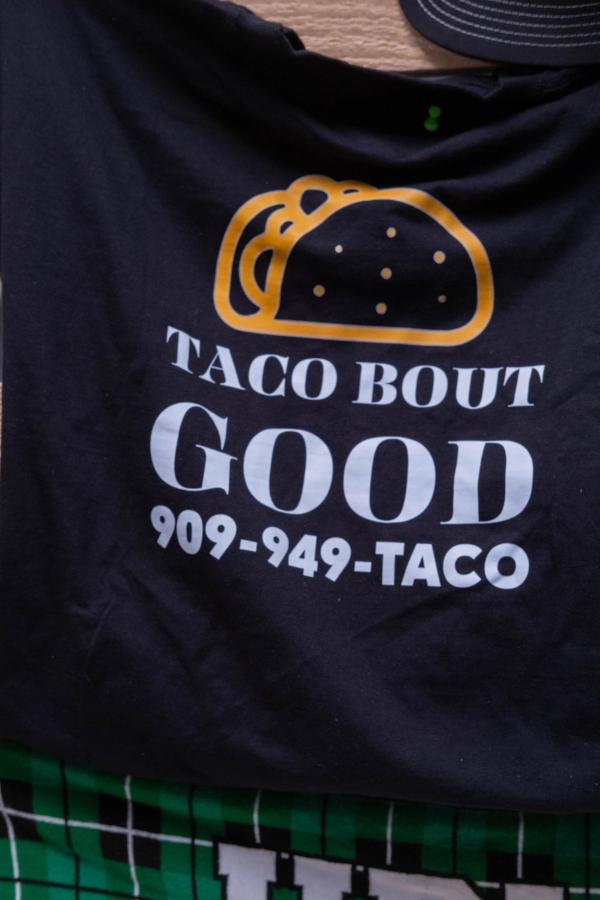 Detail of a black Taco Bout Good shirt with the logo and phone number