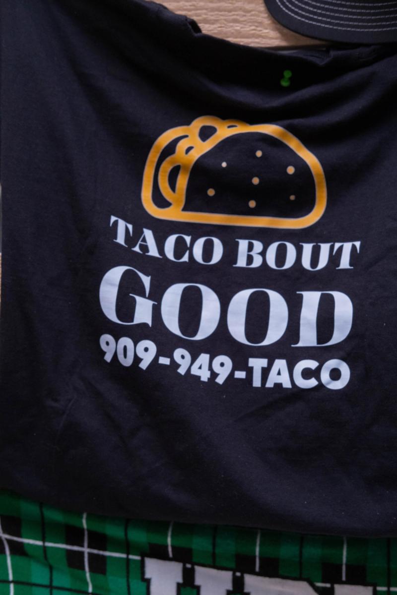 Detail of a black Taco Bout Good shirt with the logo and phone number