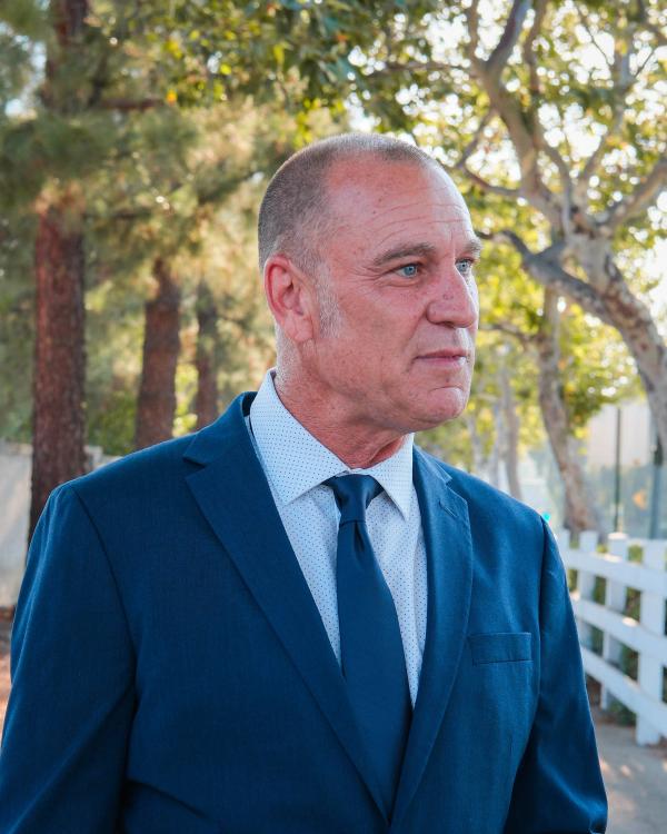 Candidate in a blue suit speaking with his hands on a tree-lined path