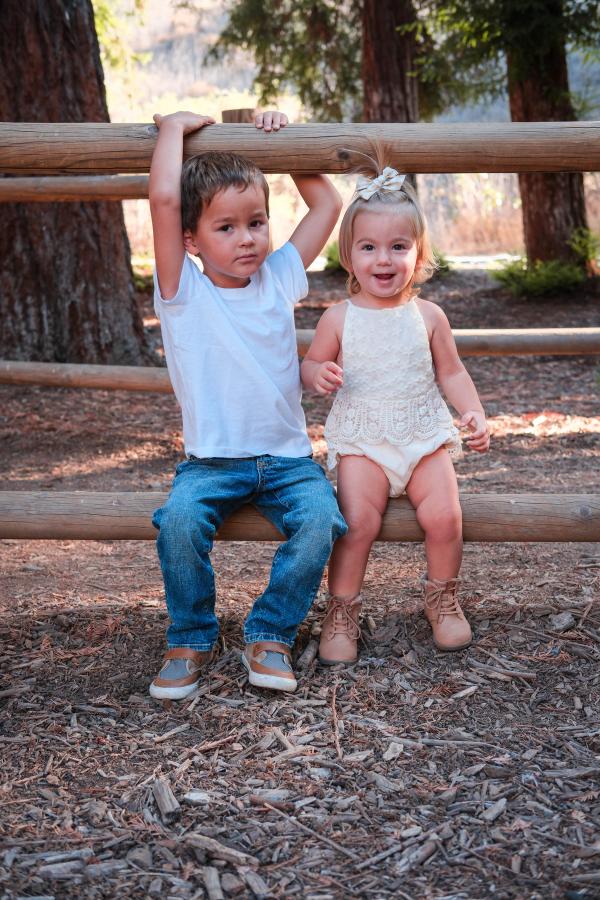 Brother and sister sitting together on a wooden fence rail in the woods