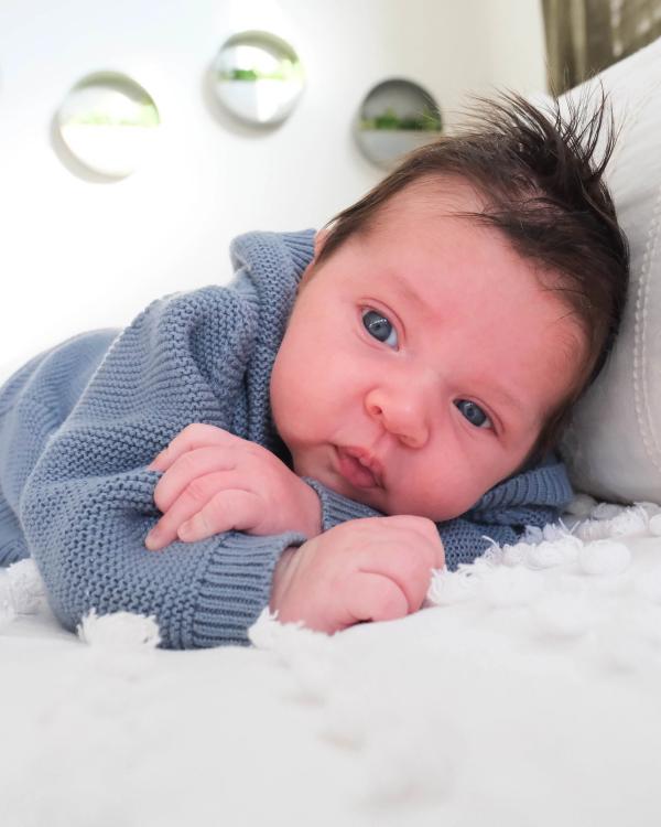 Newborn in a blue sweater lying on his tummy and looking at the camera