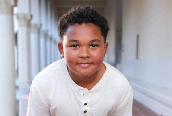 Smiling portrait of a young boy in a cream henley along a sunlit colonnade