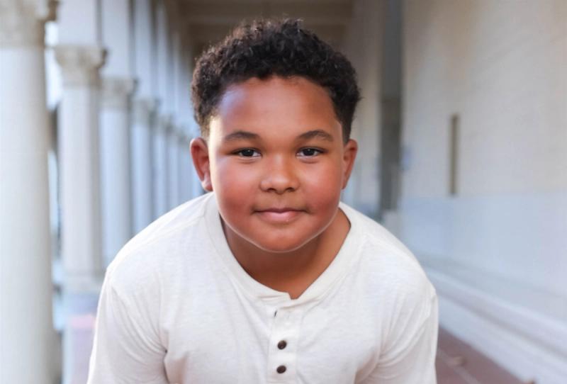 Smiling portrait of a young boy in a cream henley along a sunlit colonnade