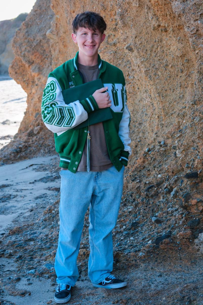 Senior in a letterman jacket standing in a rocky beach cove