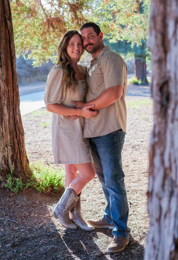 Couple holding each other among the pine trunks in evening light