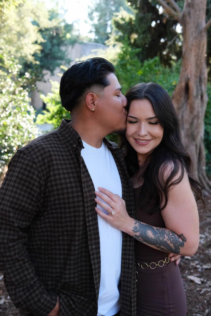 Young couple embracing among the trees, he kisses her temple