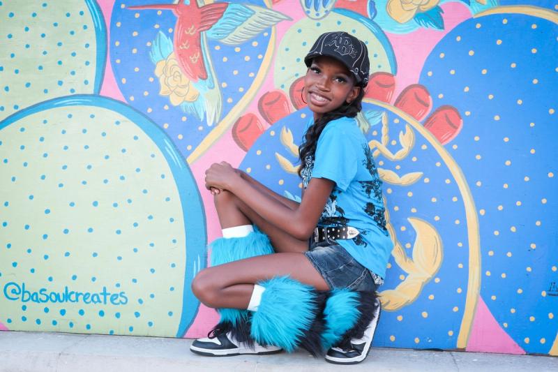 Girl crouching in her fuzzy blue boots in front of a bright mural