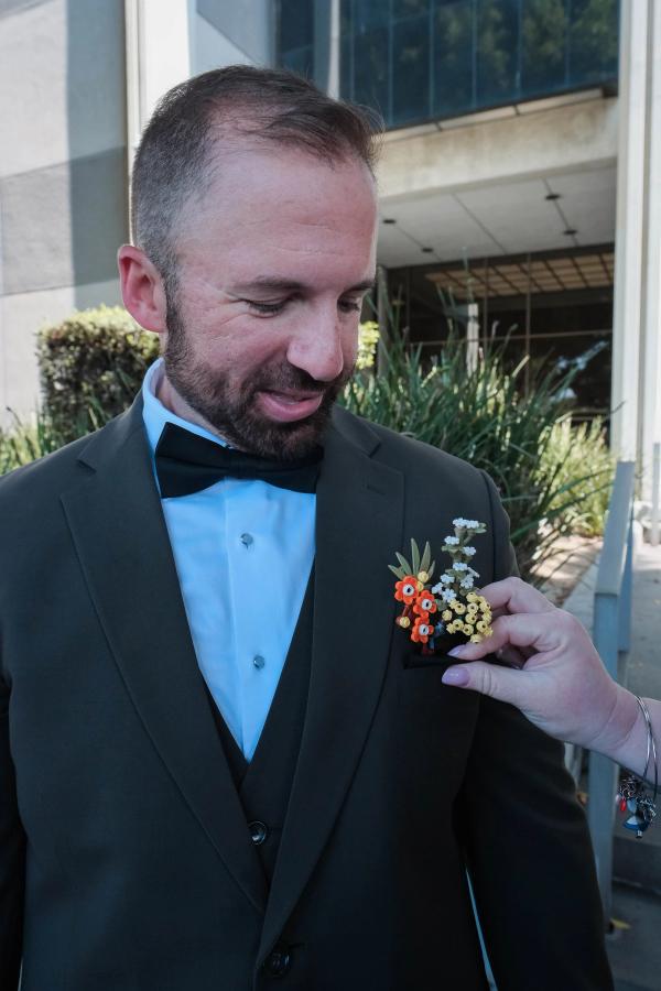 Family member pinning a bright boutonniere on a smiling groom