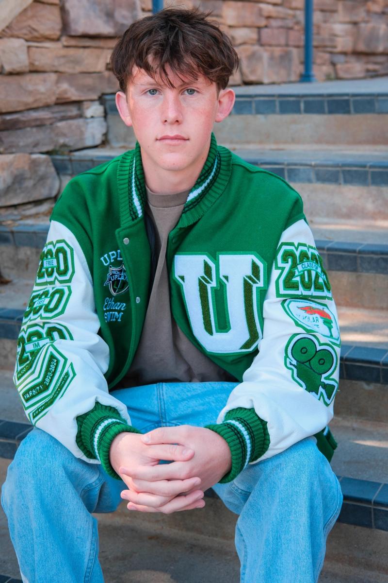 Senior in a green and white letterman jacket seated on steps, smiling
