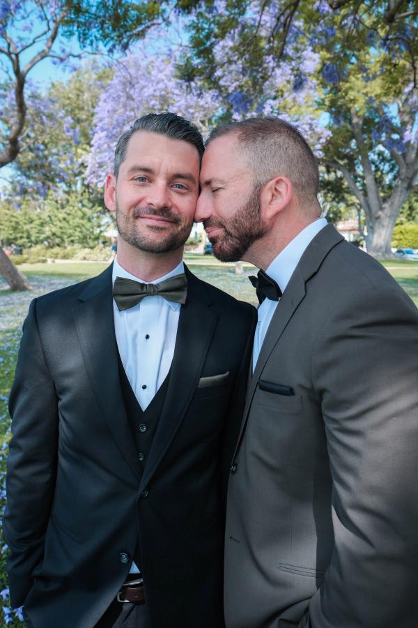 Grooms leaning in close with jacaranda blooms behind them