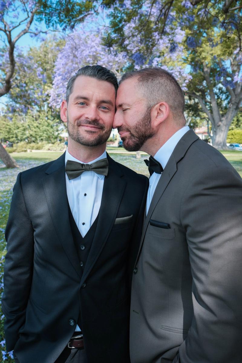 Grooms leaning in close with jacaranda blooms behind them