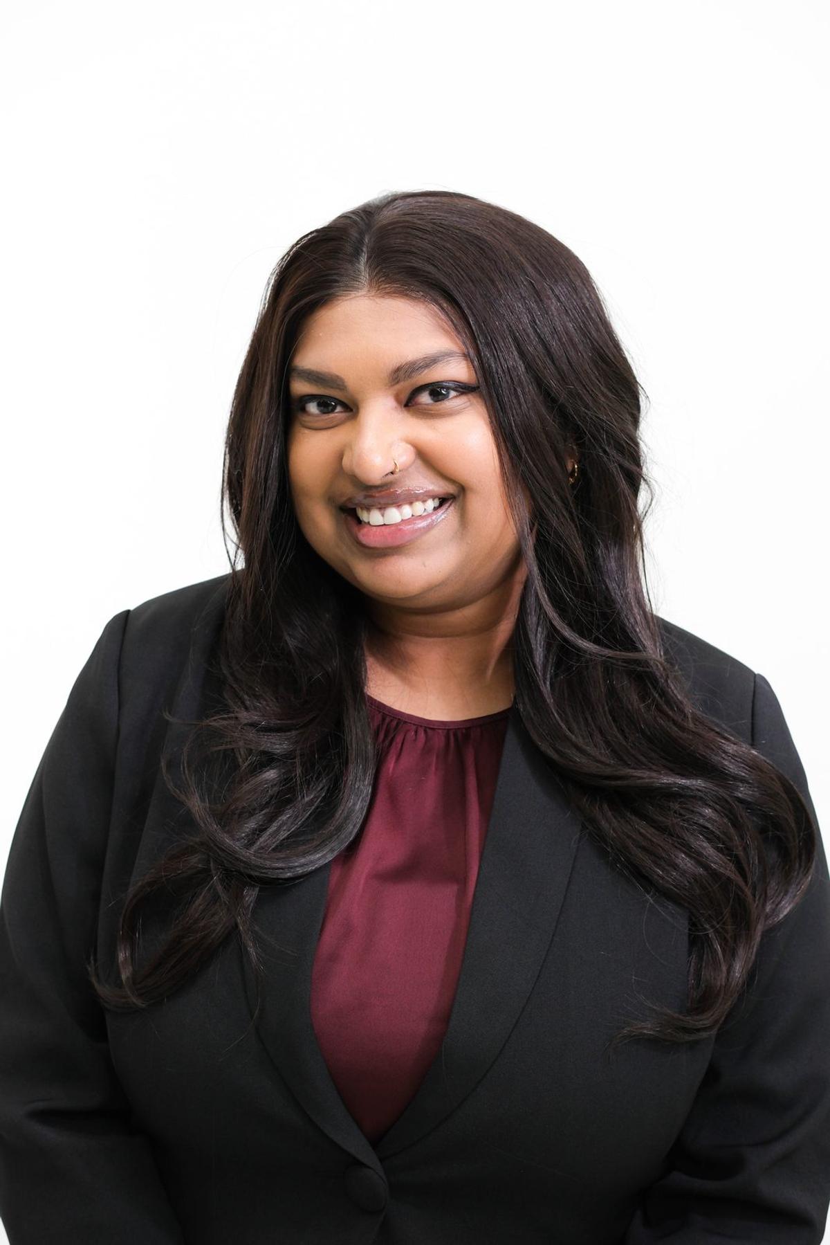 Polished studio headshot of a smiling woman in a black blazer and burgundy blouse