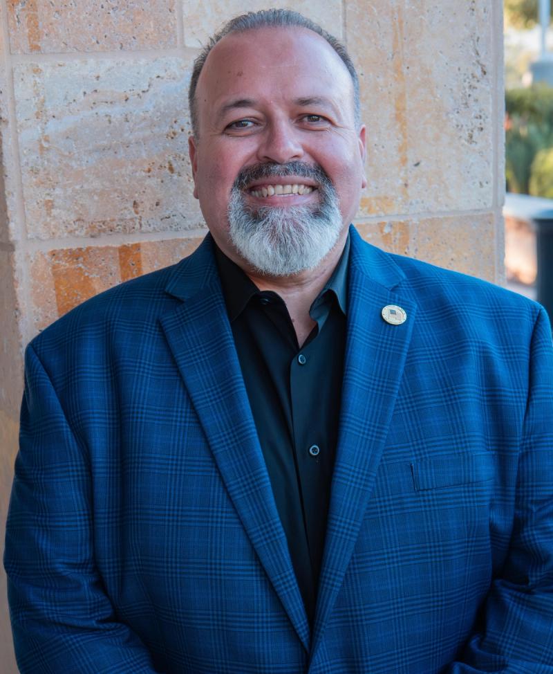 Smiling campaign headshot of a bearded man in a blue blazer