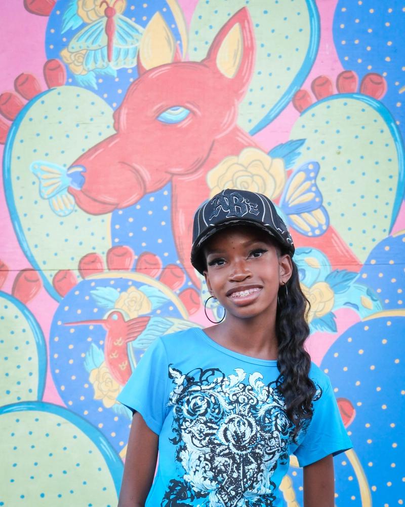 Smiling birthday girl in a sparkly cap in front of a colorful cactus mural