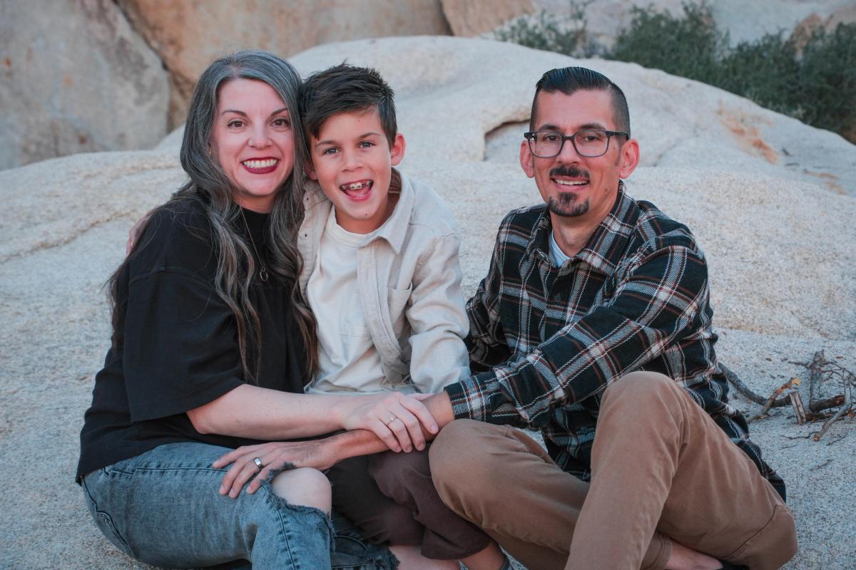 Family of three sitting close together on a sunlit boulder in Joshua Tree