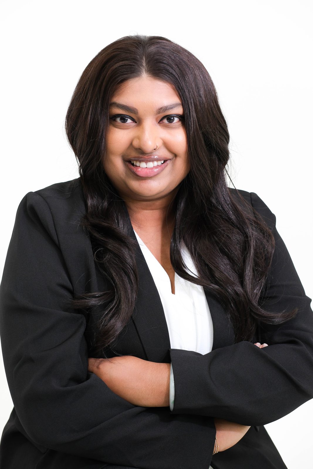 Professional woman in a black blazer and white blouse, arms crossed, smiling on a clean studio backdrop