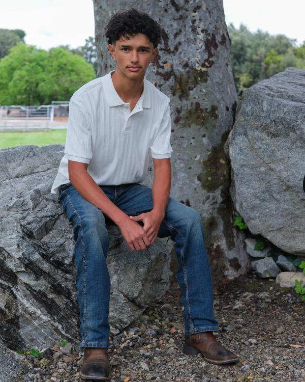 Teen in a white polo sitting on a boulder under a big oak tree