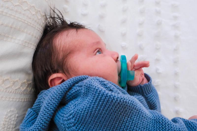 Close-up of a newborn in a blue knit sweater with a pacifier