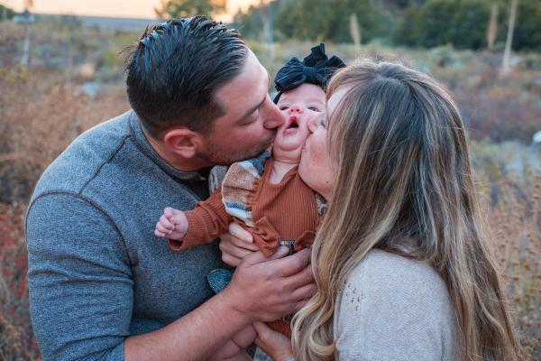 Parents kissing their baby girl on both cheeks in golden light