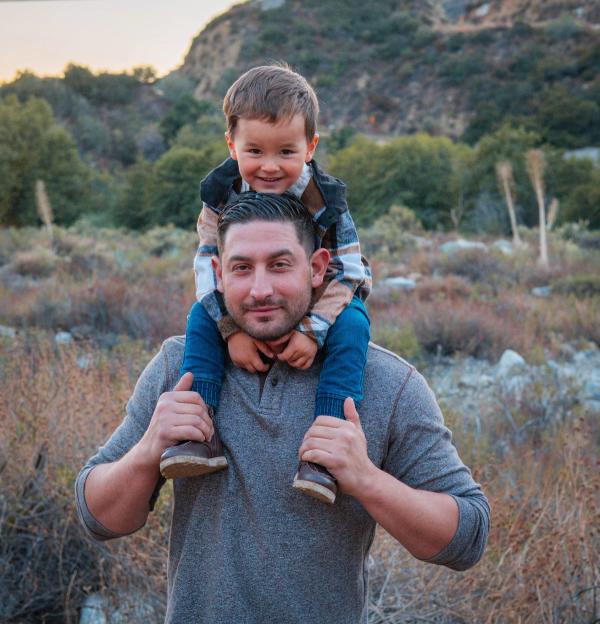 Little boy in a plaid shirt riding on his dad’s shoulders