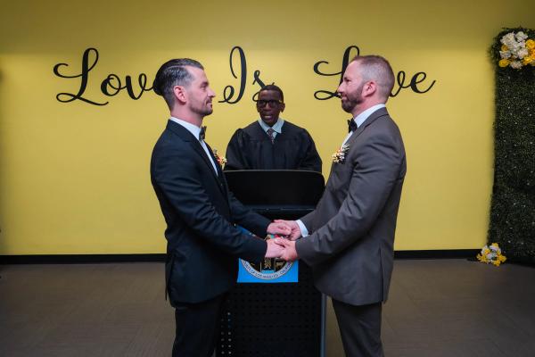 Grooms holding hands at the podium in front of a Love Is Love wall