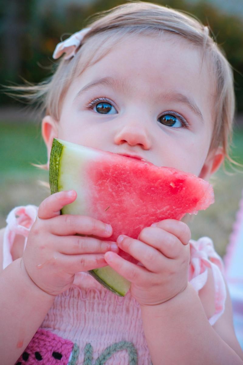 Close-up of a baby with big blue eyes biting into a watermelon slice