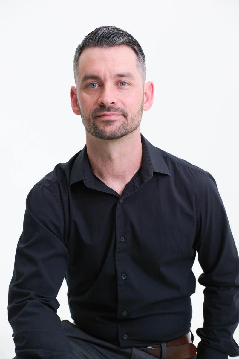 Seated studio portrait of a man in a black button-down shirt