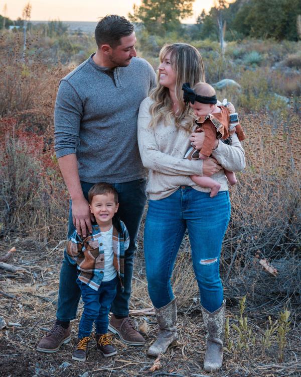 Family of four standing together in tall golden grass at sunset