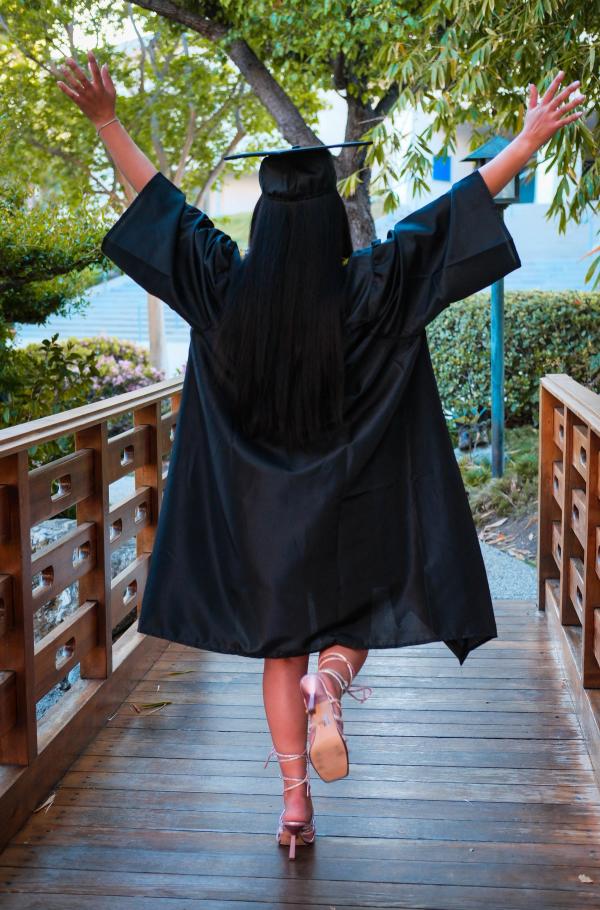 Graduate with arms raised in triumph walking across a bridge