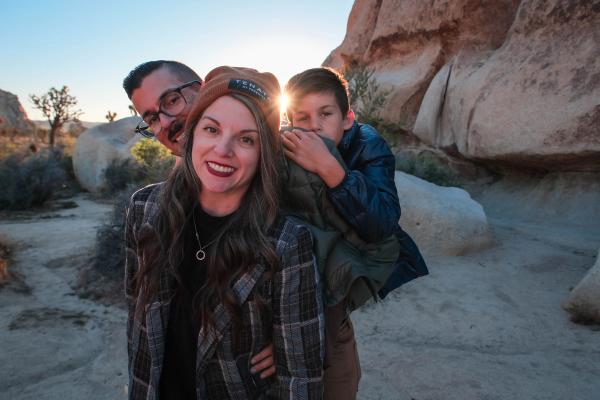Family of three hugging in the desert as the sun bursts over the boulders