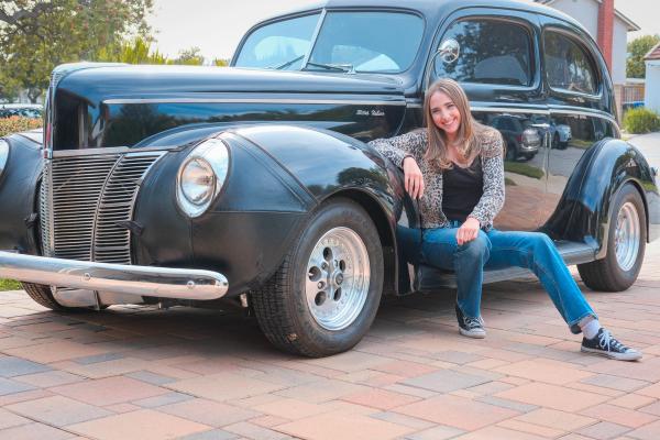 Young woman sitting on the running board of a vintage black car