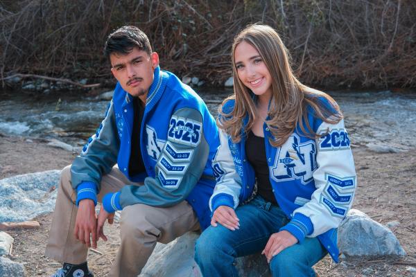 Senior siblings in letterman jackets sitting on a boulder by the water