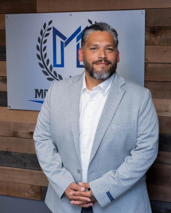 Smiling team member in a light gray blazer in front of the company logo