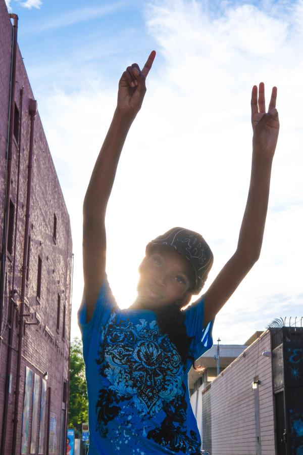 Birthday girl raising peace signs to the sky in a sunlit alley